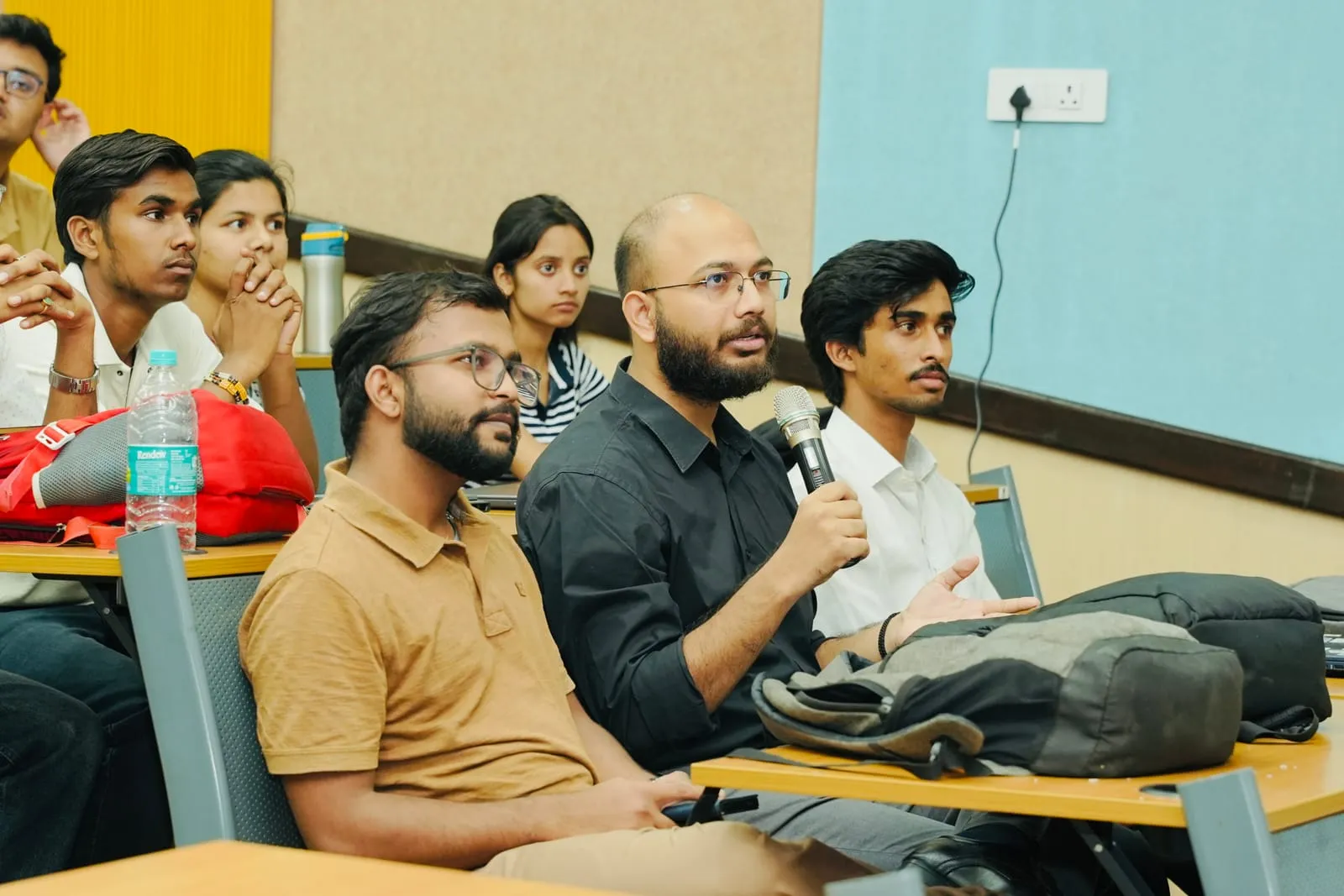 An attendee speaking into a microphone from the lecture hall seats, the people around him listening