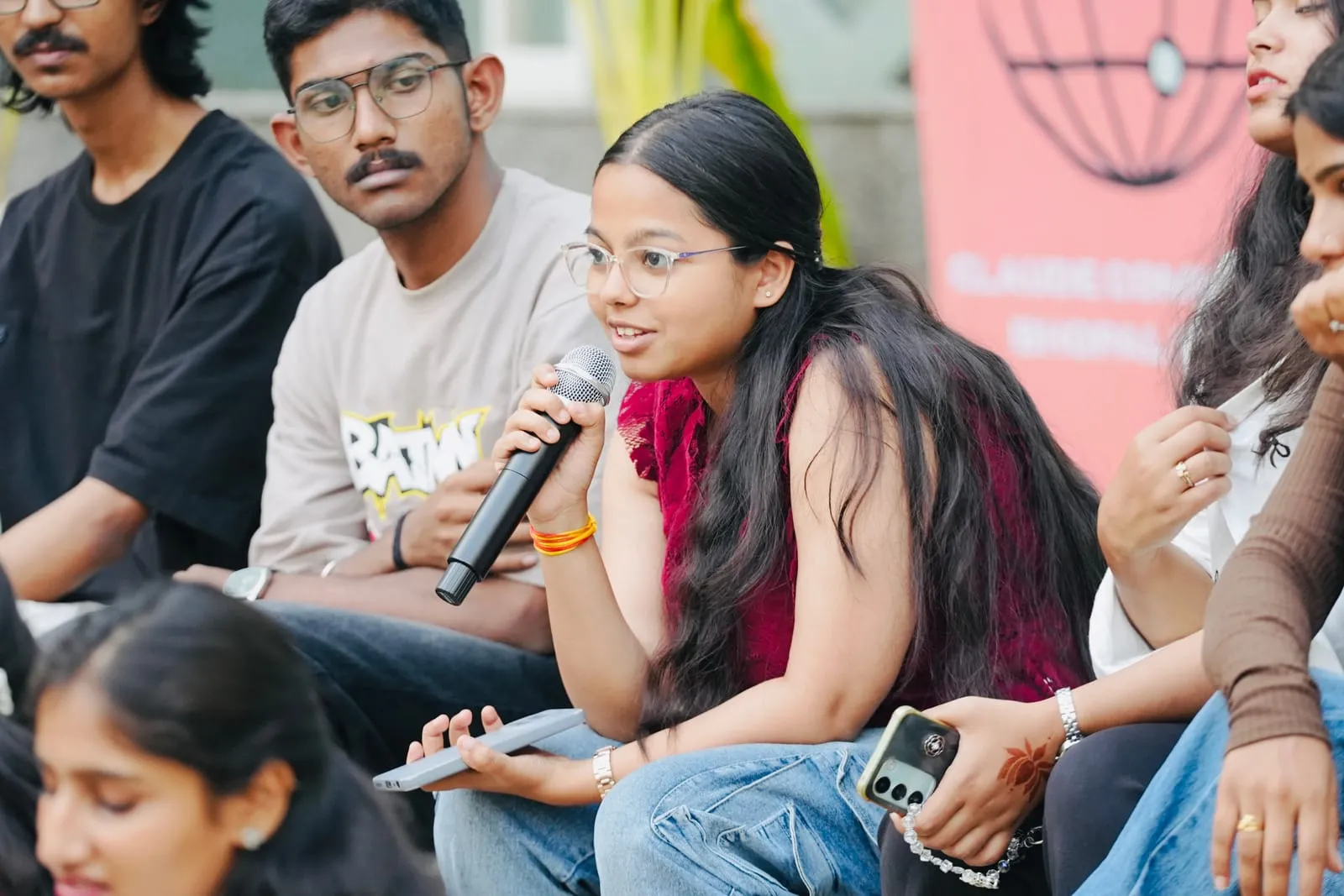 An attendee in a red top speaking into a microphone from among the seated audience