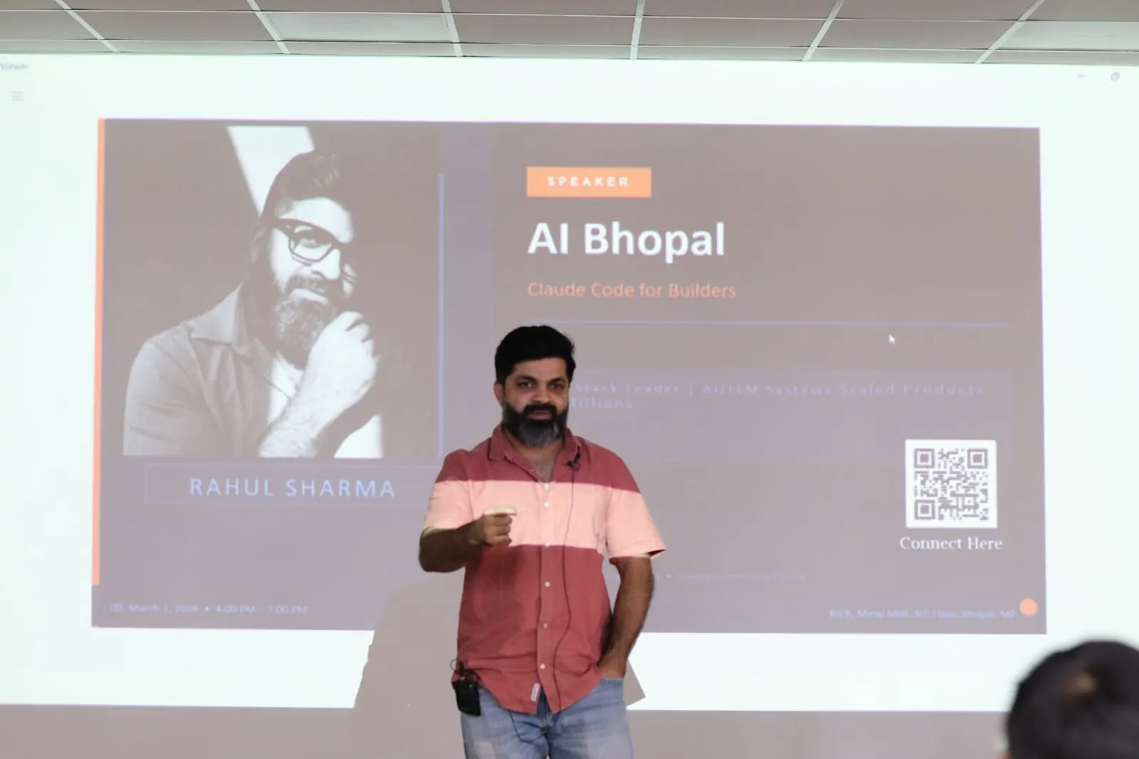 A speaker in a striped shirt presenting in front of the projected speaker card for Claude Code for Builders