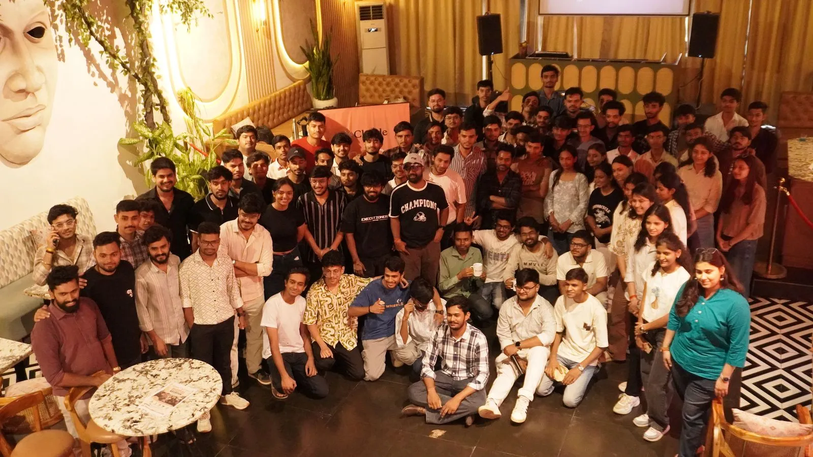 Attendees of the Claude Meetup posing for a group photo in a lounge venue in Bhopal, with the orange Claude standee behind them