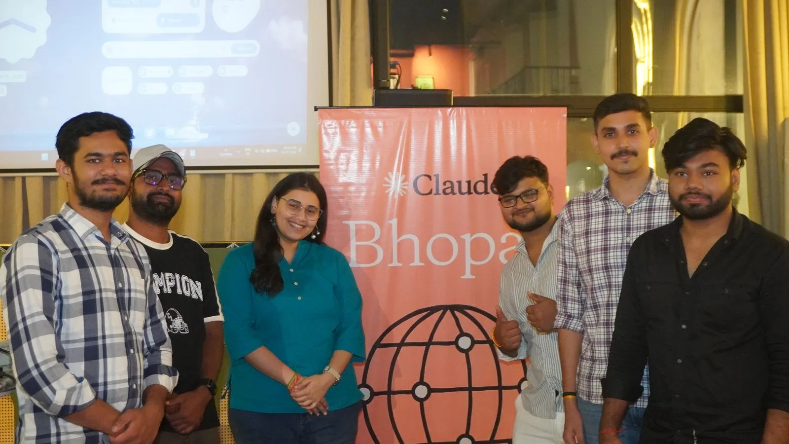Six organisers and volunteers standing beside the orange Claude Bhopal roll-up standee at the Claude Meetup