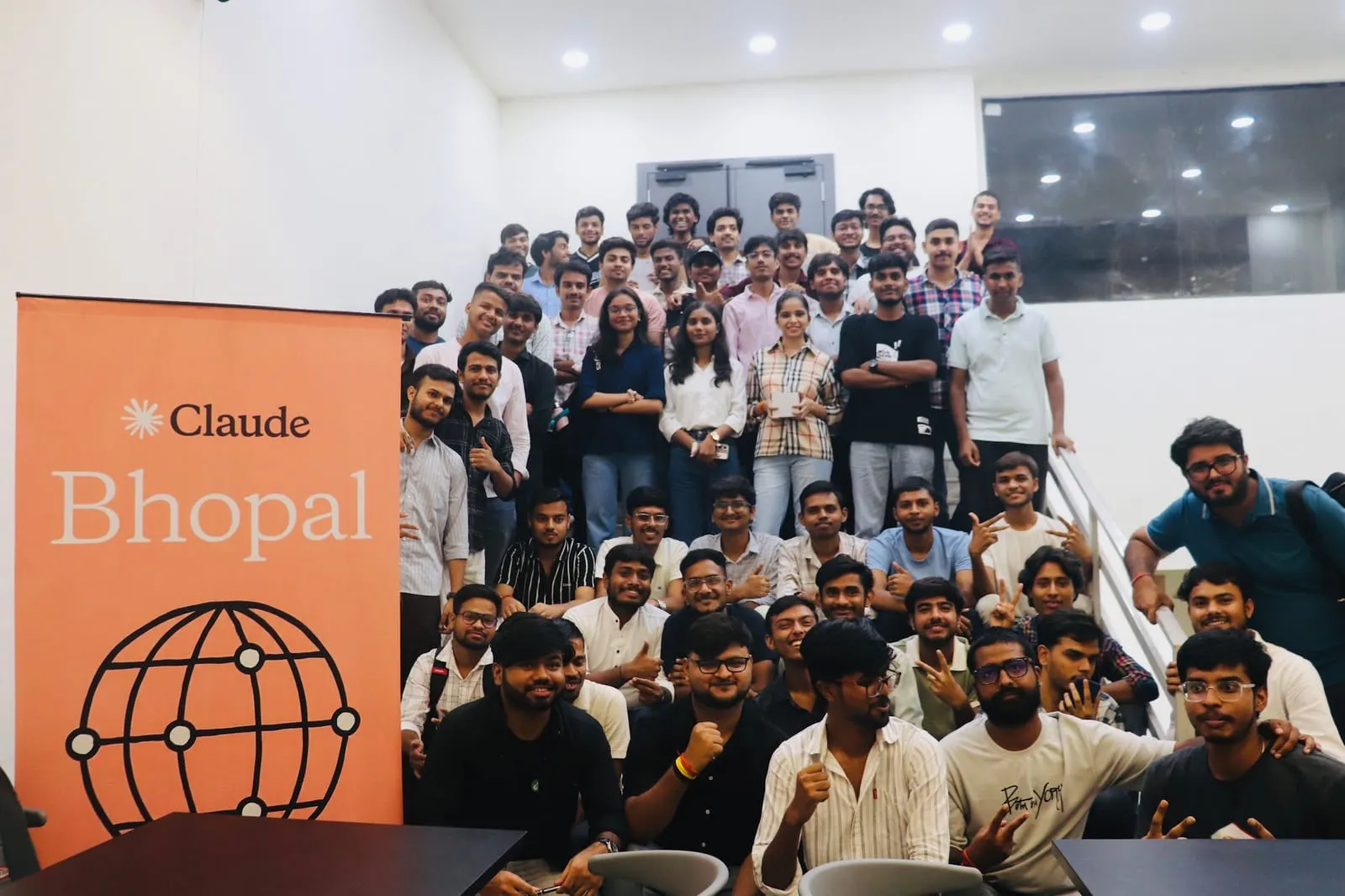 Attendees of the Claude Community Conversation posing on a staircase beside the orange Claude Bhopal banner