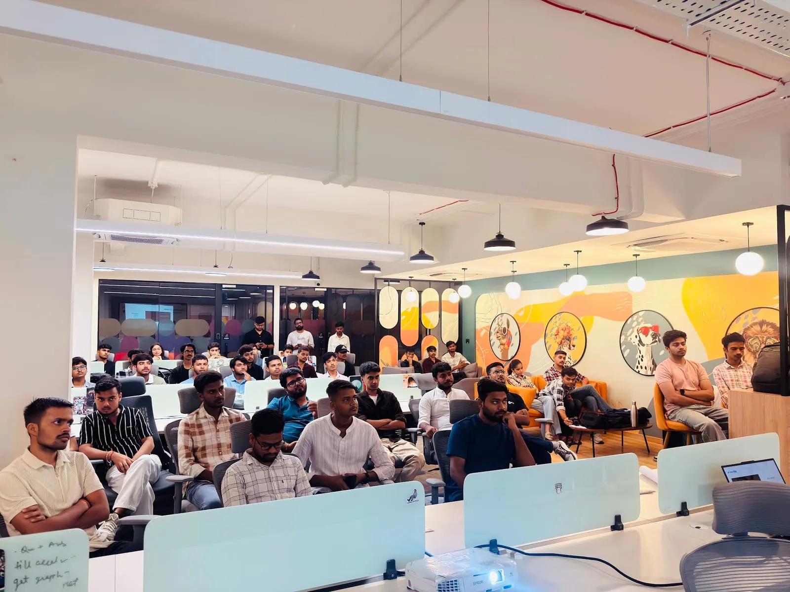 Attendees seated across a coworking room with a colourful mural wall, facing the front