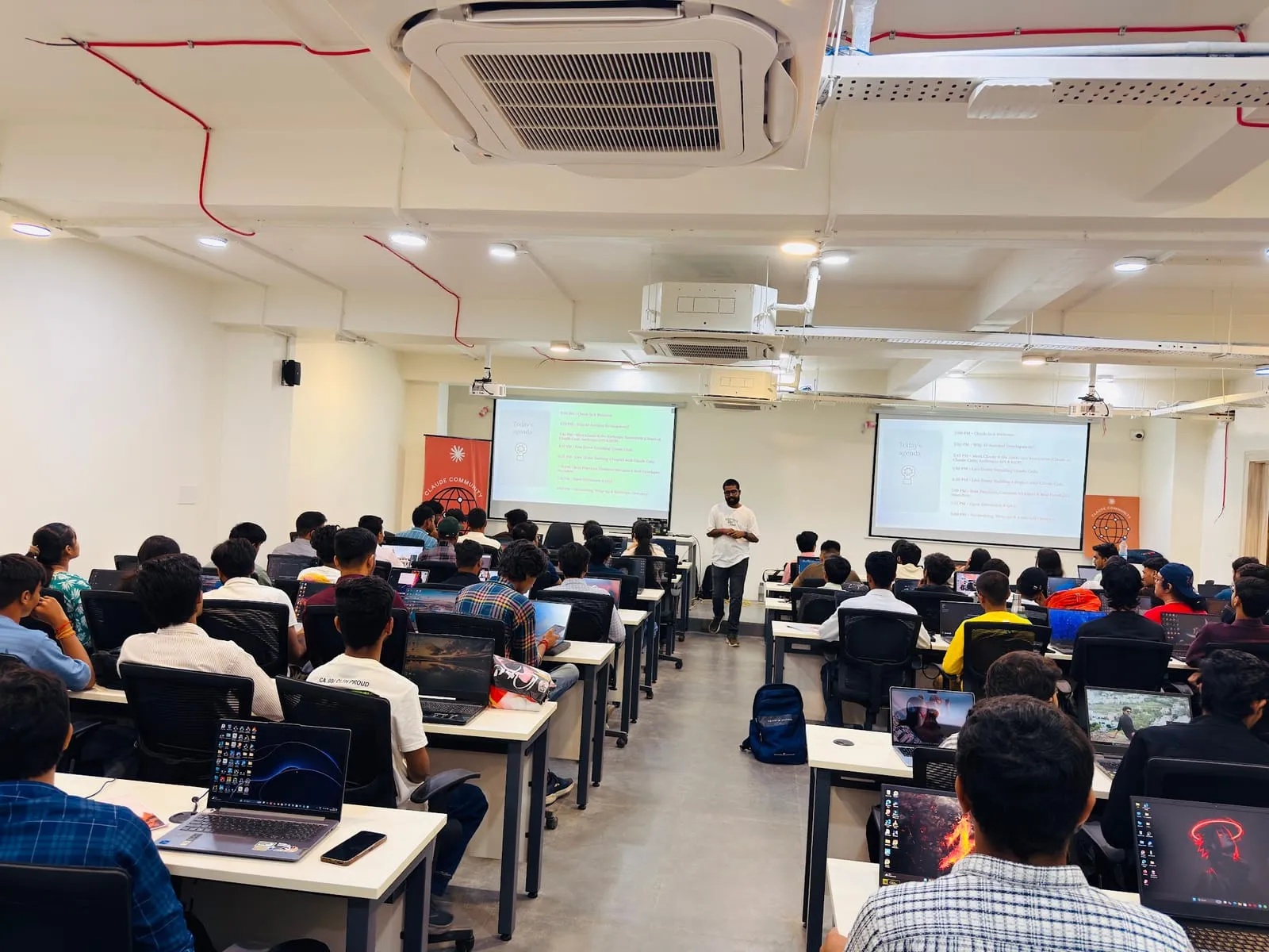Rows of participants working on laptops in the lab classroom, with slides and code on the two screens at the front