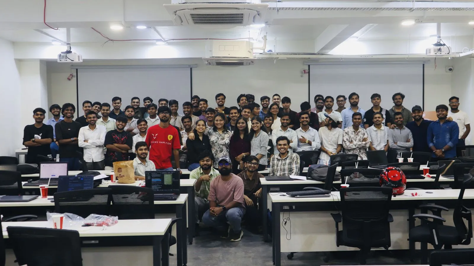 Around sixty participants standing among the desks of the classroom venue at the Claude Code Workshop in Bhopal