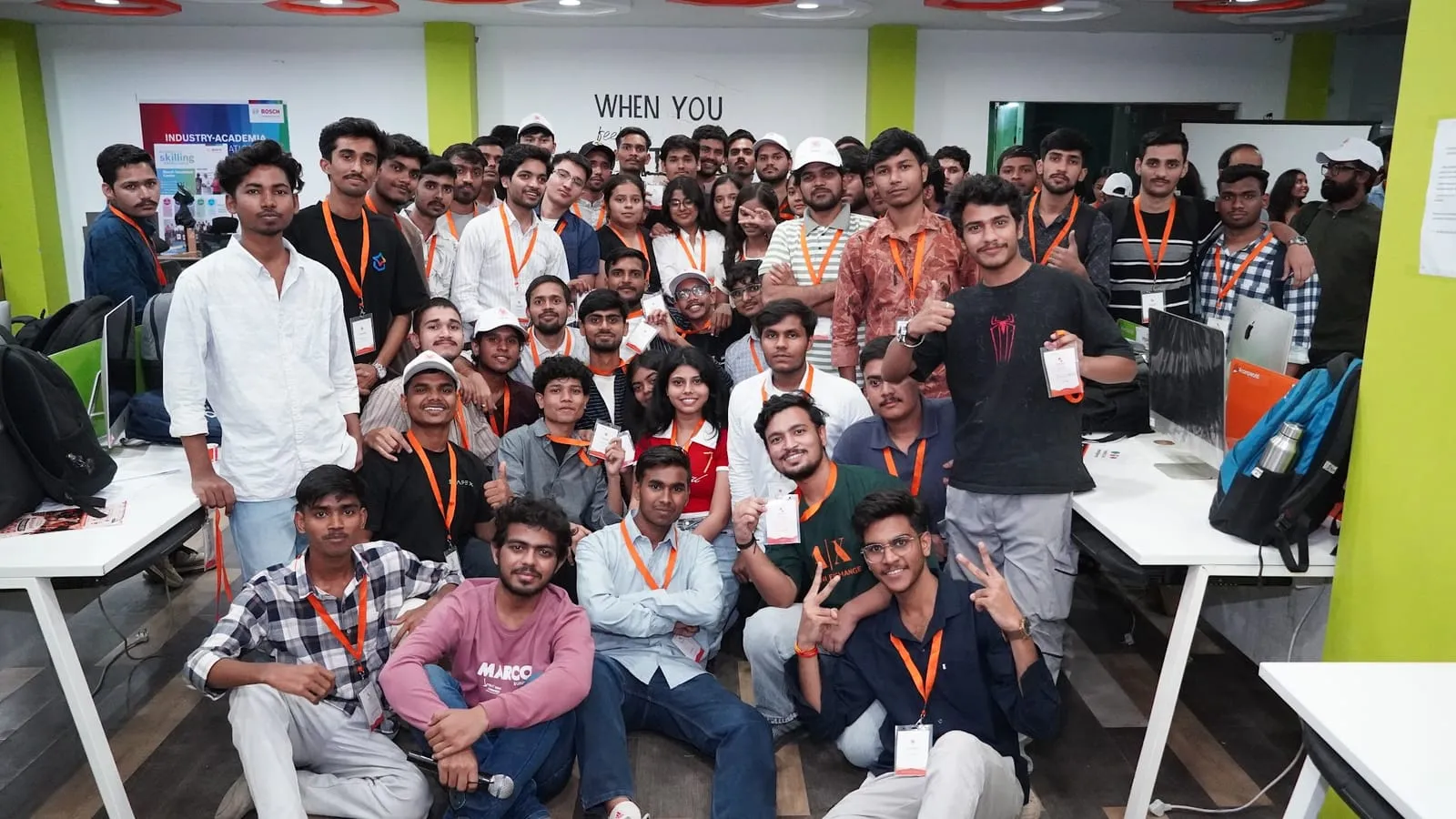 Impact Lab participants in orange lanyards crowding together for a group photo in the hackathon workspace
