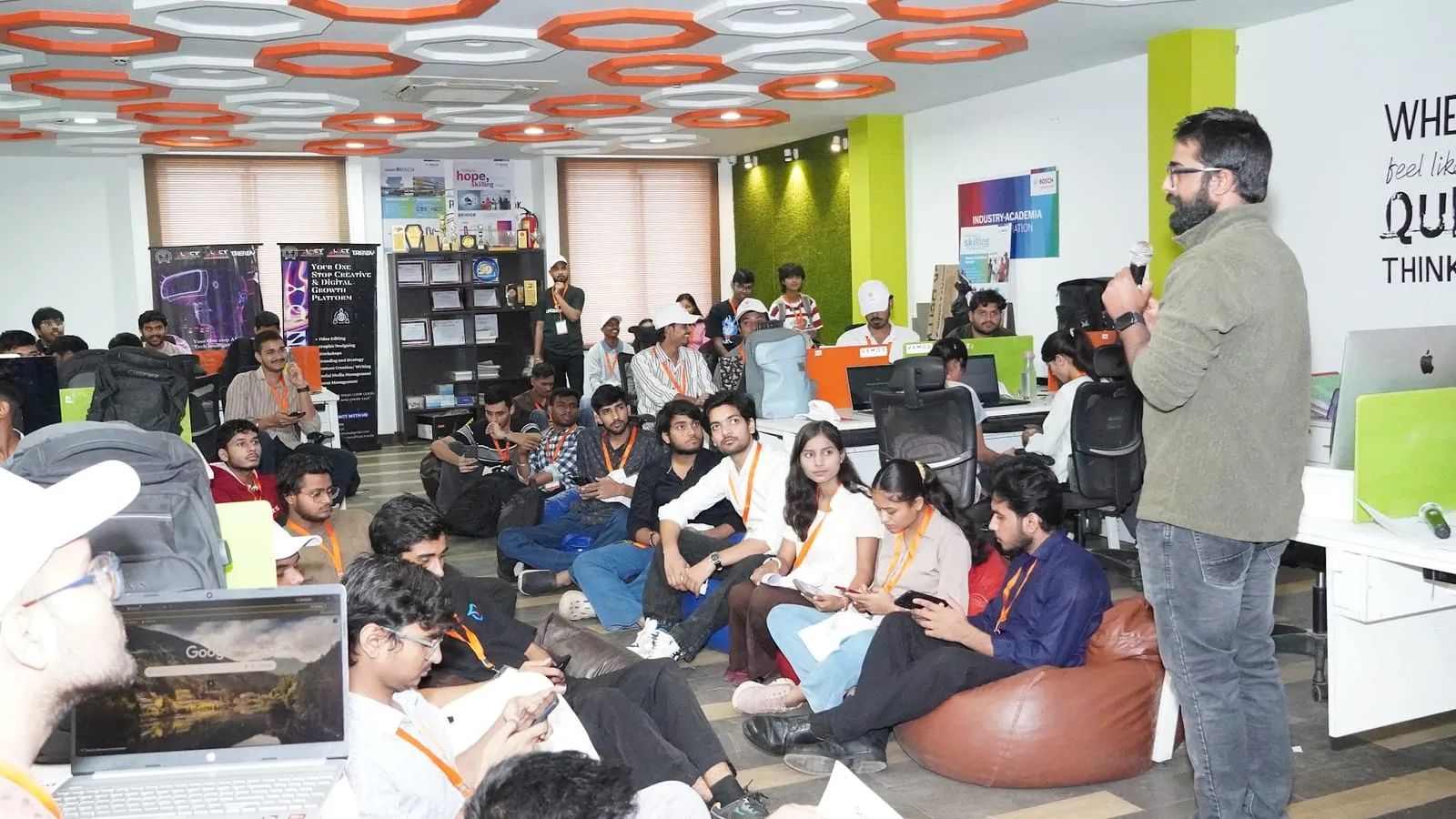 A speaker with a microphone addressing participants on beanbags and the floor of the hackathon workspace