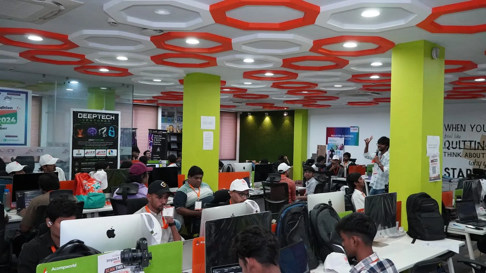 Teams building at iMacs and laptops under the orange hexagon ceiling of the workspace