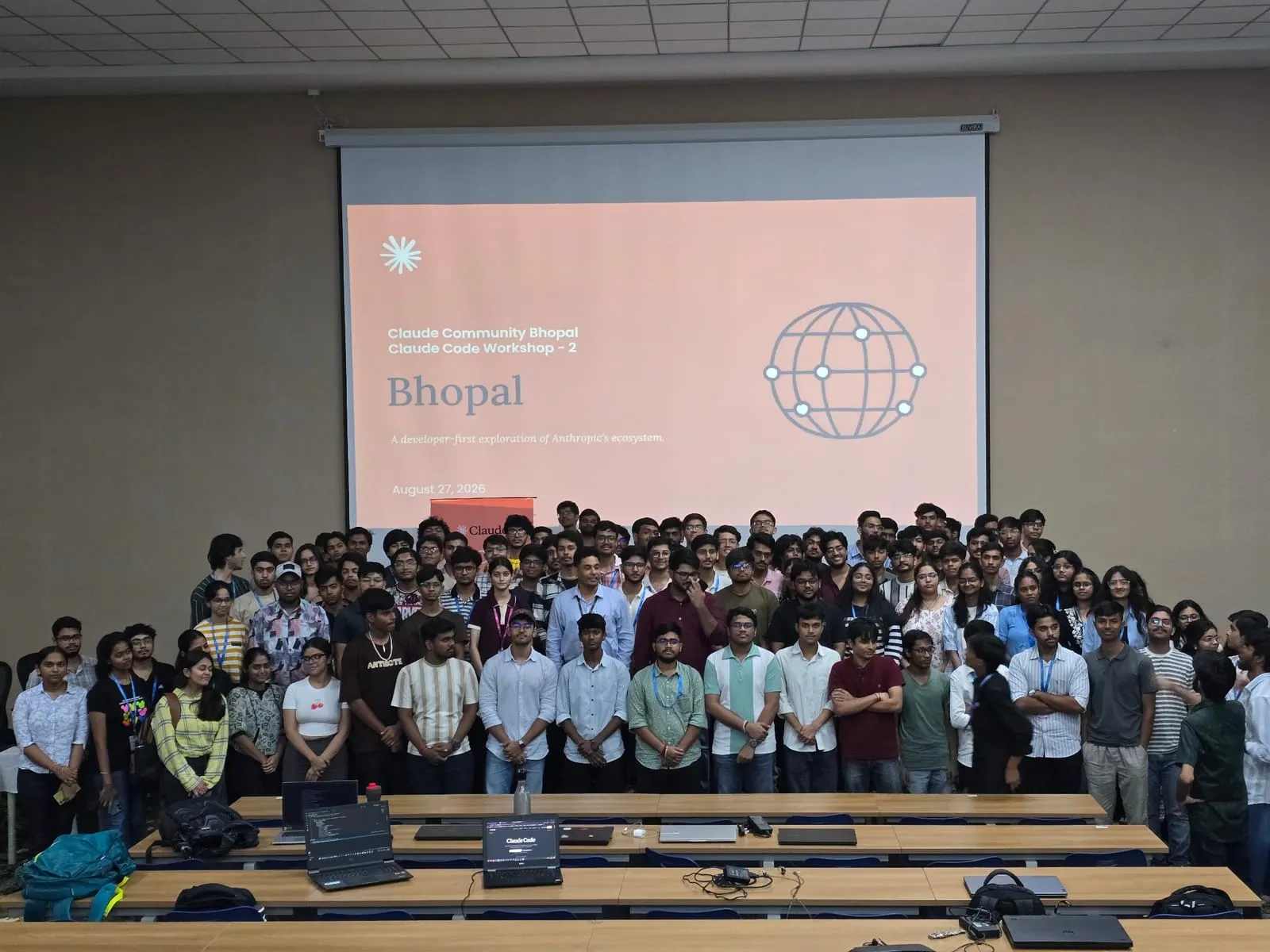 Students gathered for a group photo at the front of a college auditorium, under the Claude Community Bhopal workshop slide