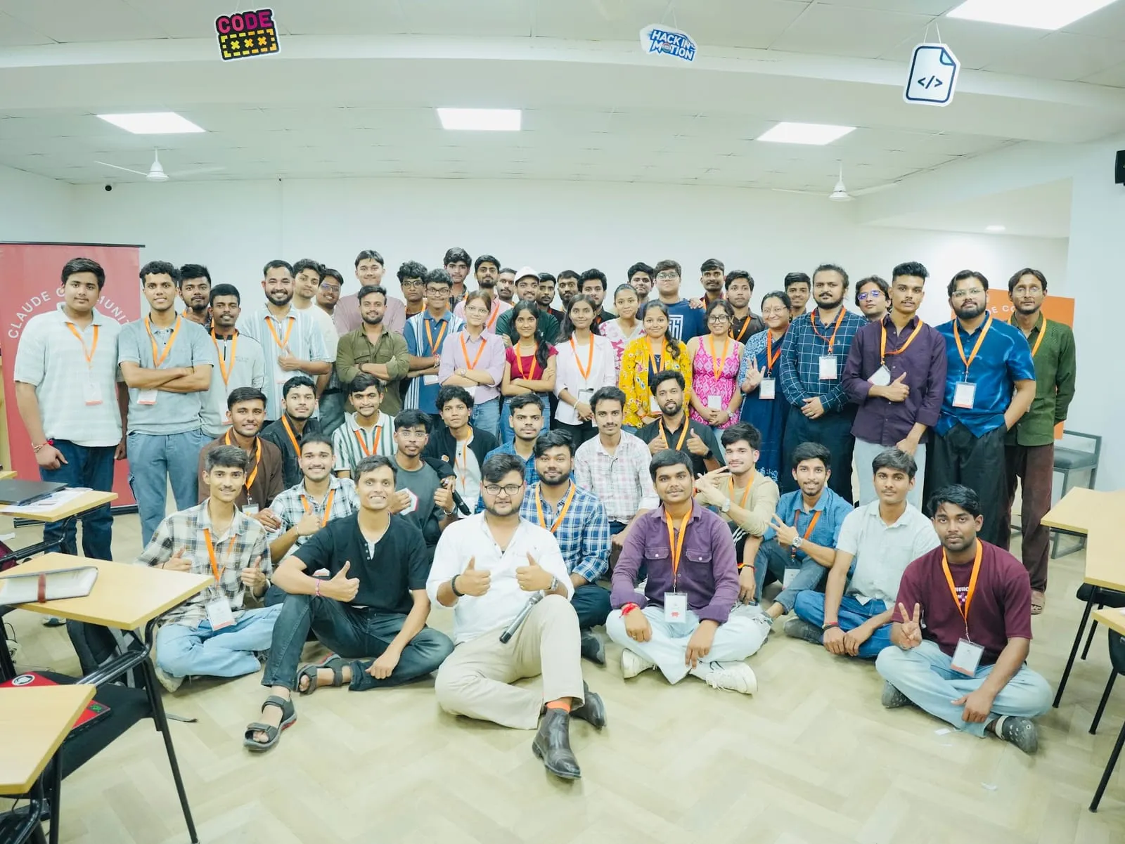 Impact Lab participants in orange lanyards posing for a group photo, the front rows sitting on the floor