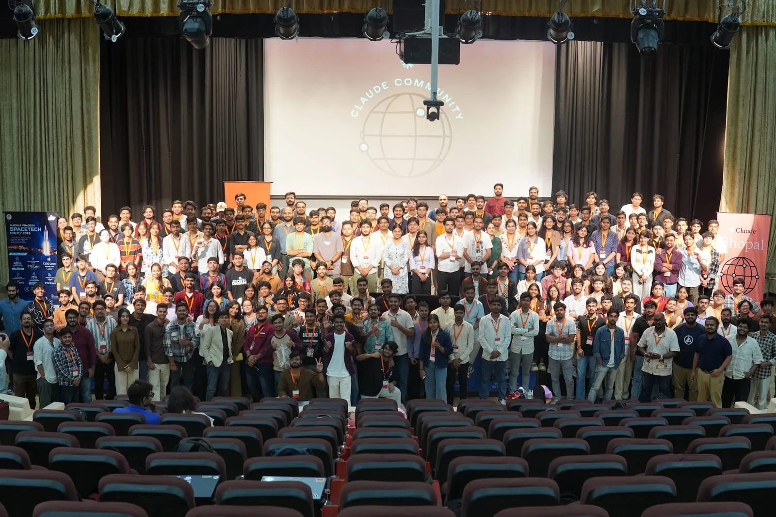 Hundreds of Build Day participants filling the front of an auditorium for a group photo, under the Claude Community title screen