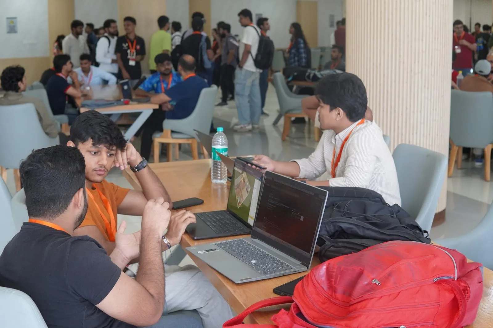 Teams working on laptops at tables in the open hall of the venue
