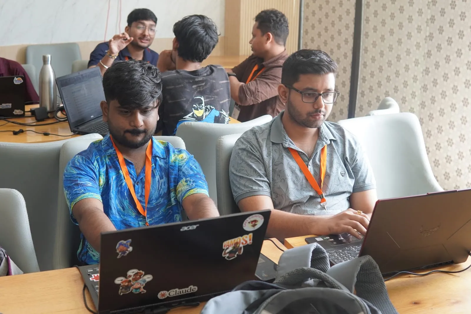 Two builders coding side by side, one laptop covered in stickers including a Claude sticker