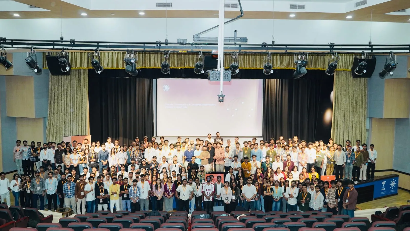 A large group of Impact Lab participants posing for a group photo in front of the stage