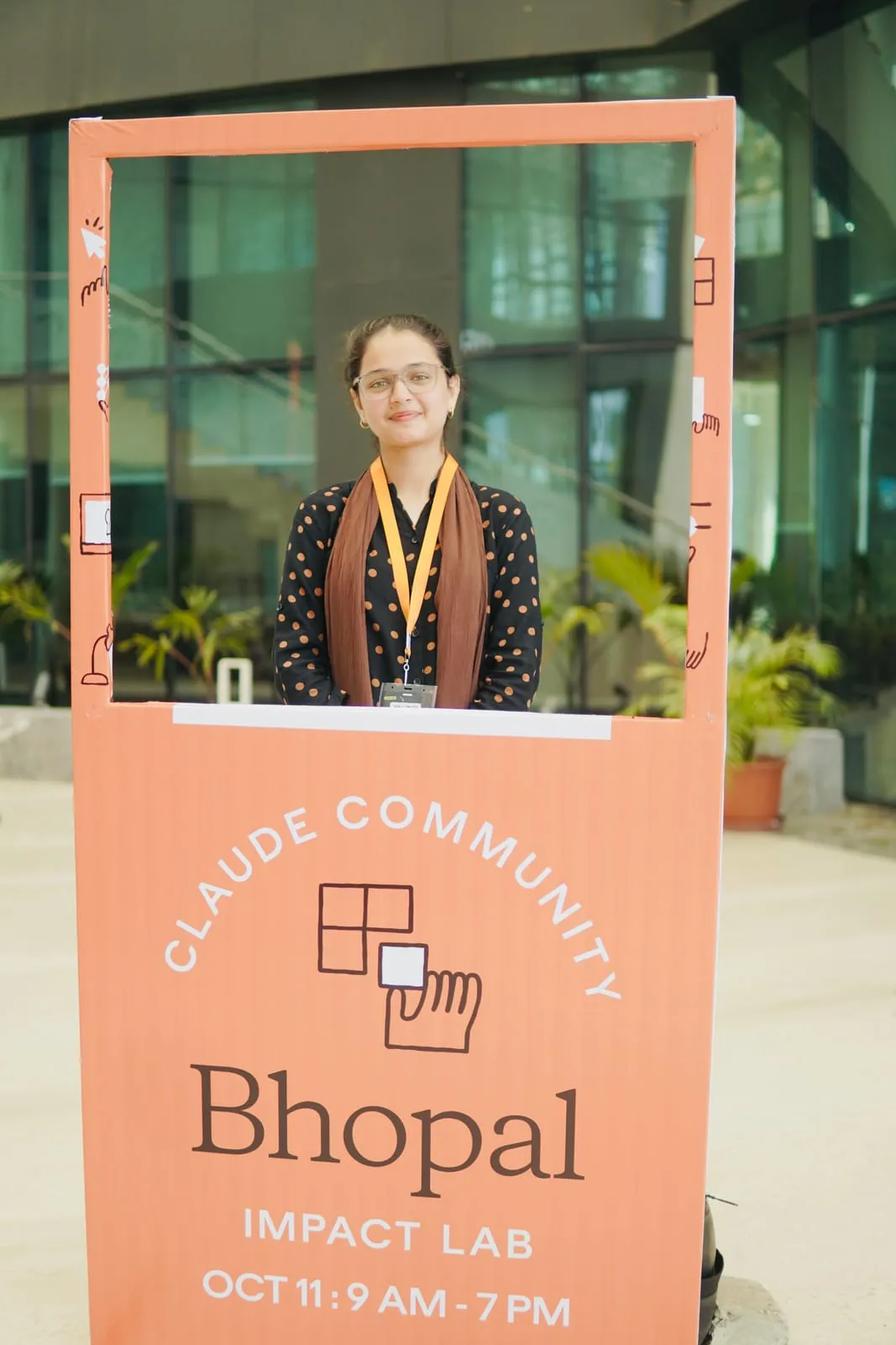 A participant in an orange lanyard posing in the Claude Community Bhopal Impact Lab photo frame, which reads Oct 11, 9 AM to 7 PM