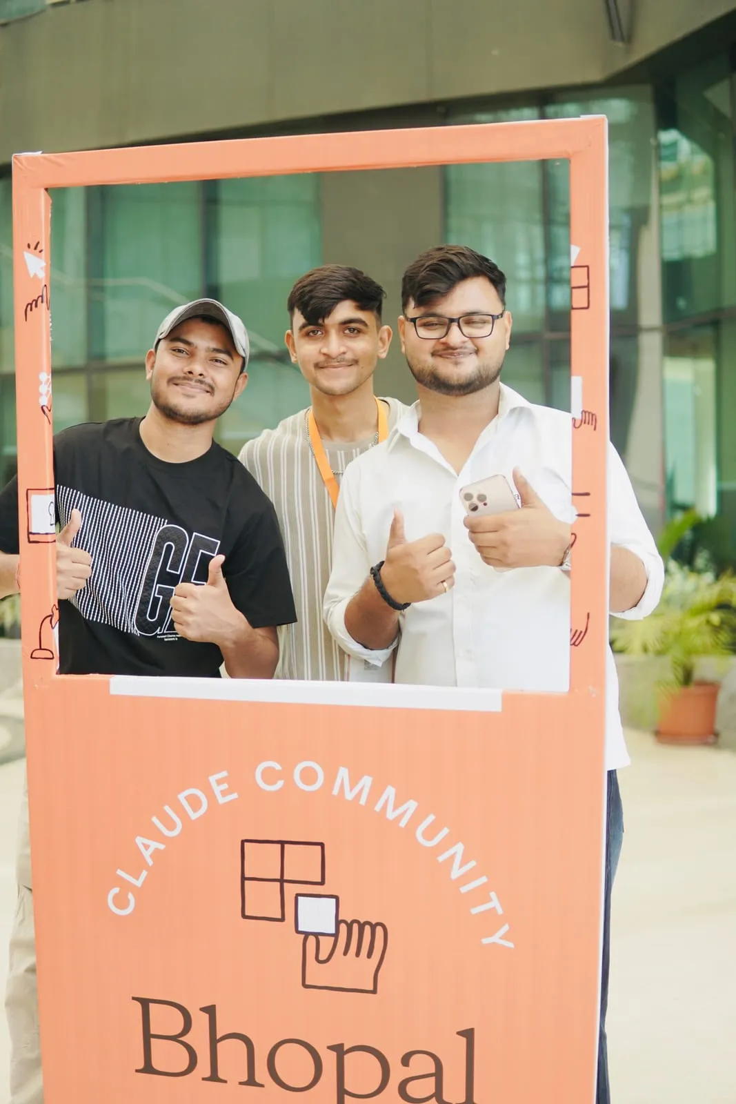 Three participants giving a thumbs up inside the Claude Community Bhopal photo frame