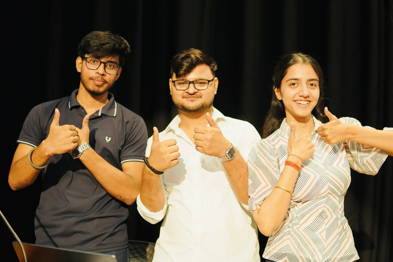 Three people giving a thumbs up in front of the stage curtain