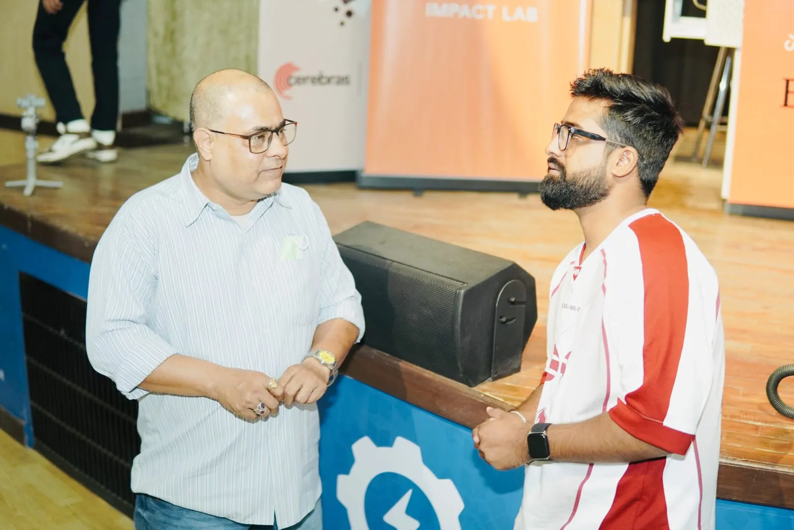 Two people in conversation by the stage, in front of the Claude Community Bhopal Impact Lab banners