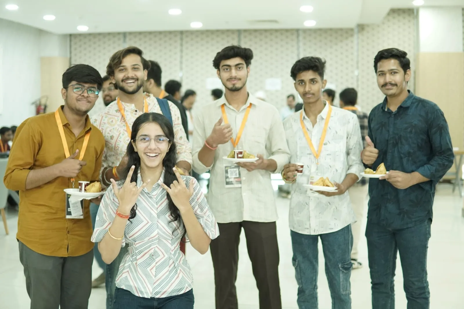 Participants in orange lanyards holding plates of snacks and cups, giving a thumbs up