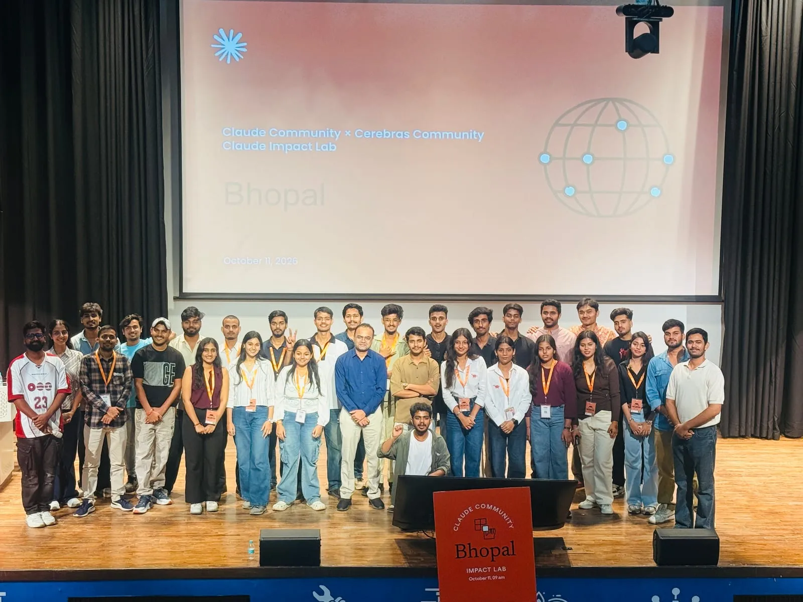 Participants in orange lanyards posing for a group photo on stage under the Claude Impact Lab slide