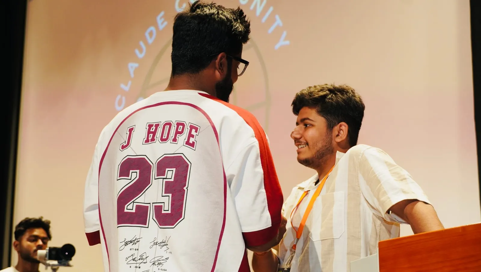 A speaker in a number 23 jersey greeting a participant in an orange lanyard on stage
