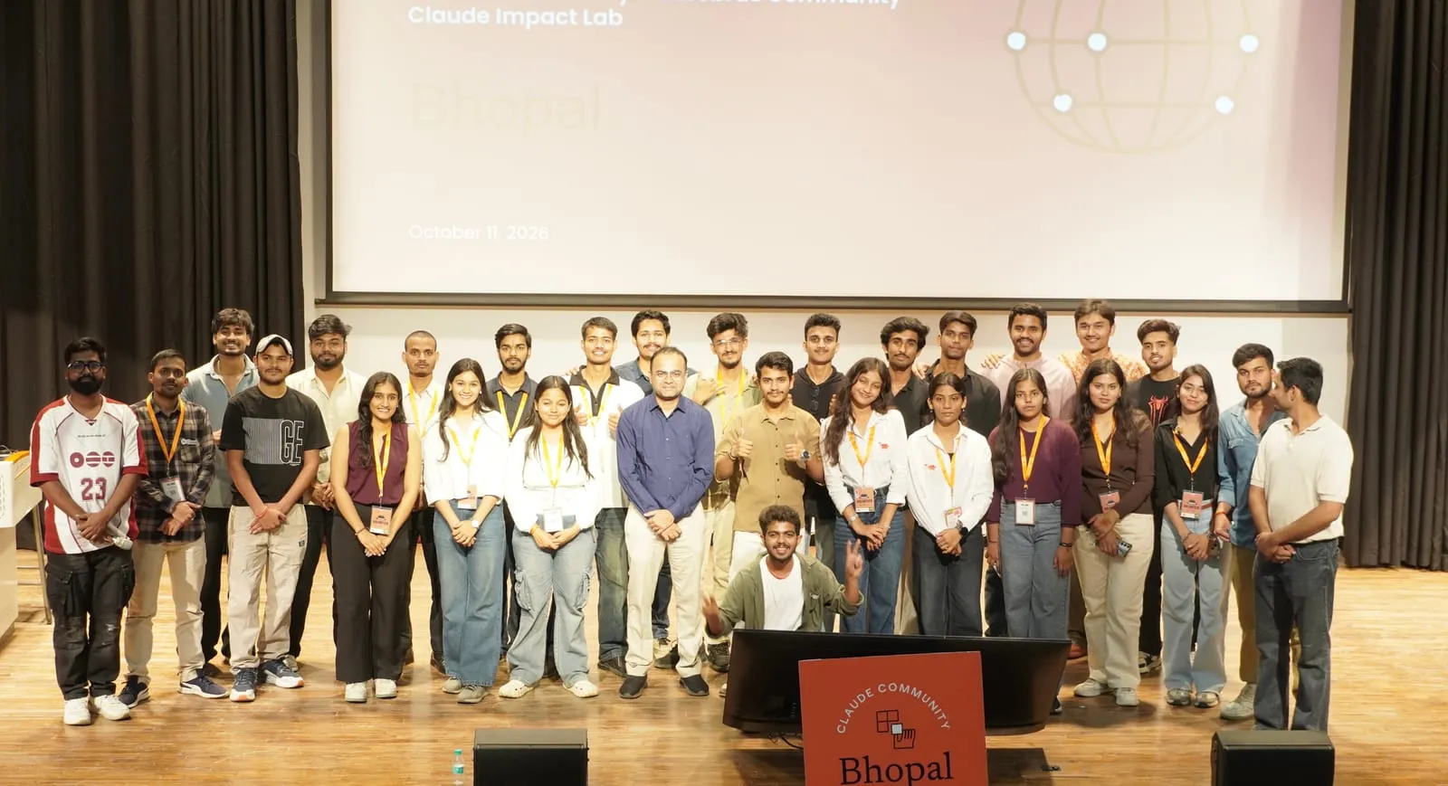 Participants posing for a group photo on stage under the October 11, 2026 Claude Impact Lab Bhopal slide