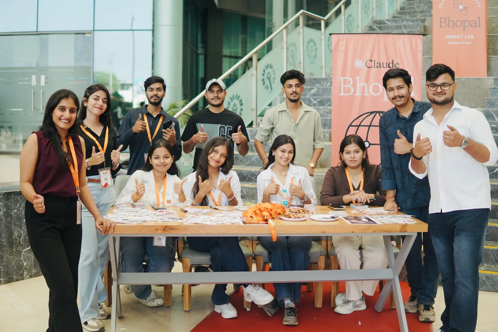 The registration team in orange lanyards giving a thumbs up at the desk, under a Claude Bhopal banner