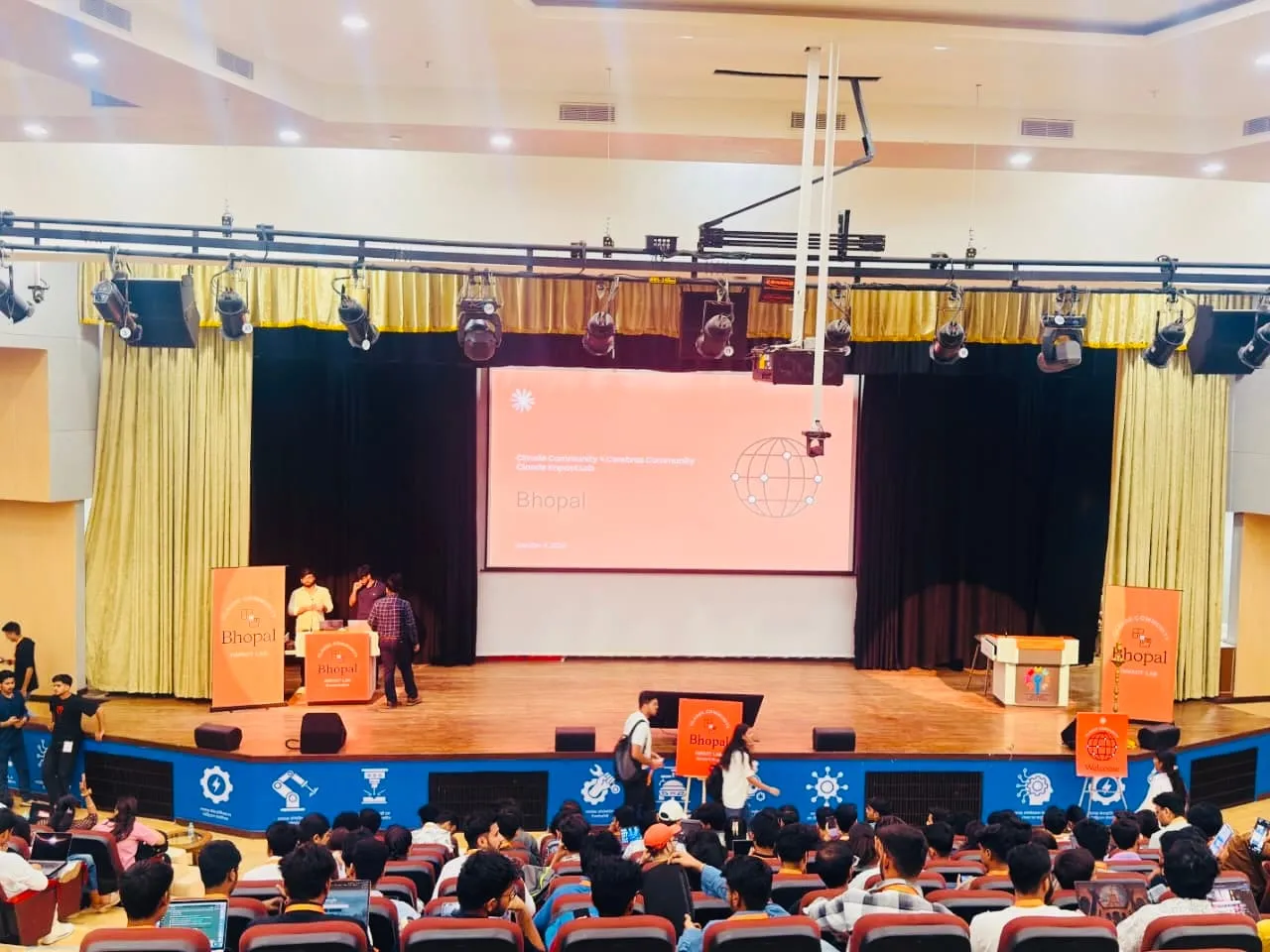 The auditorium filling up under the Claude Impact Lab Bhopal slide, participants at laptops in the front rows